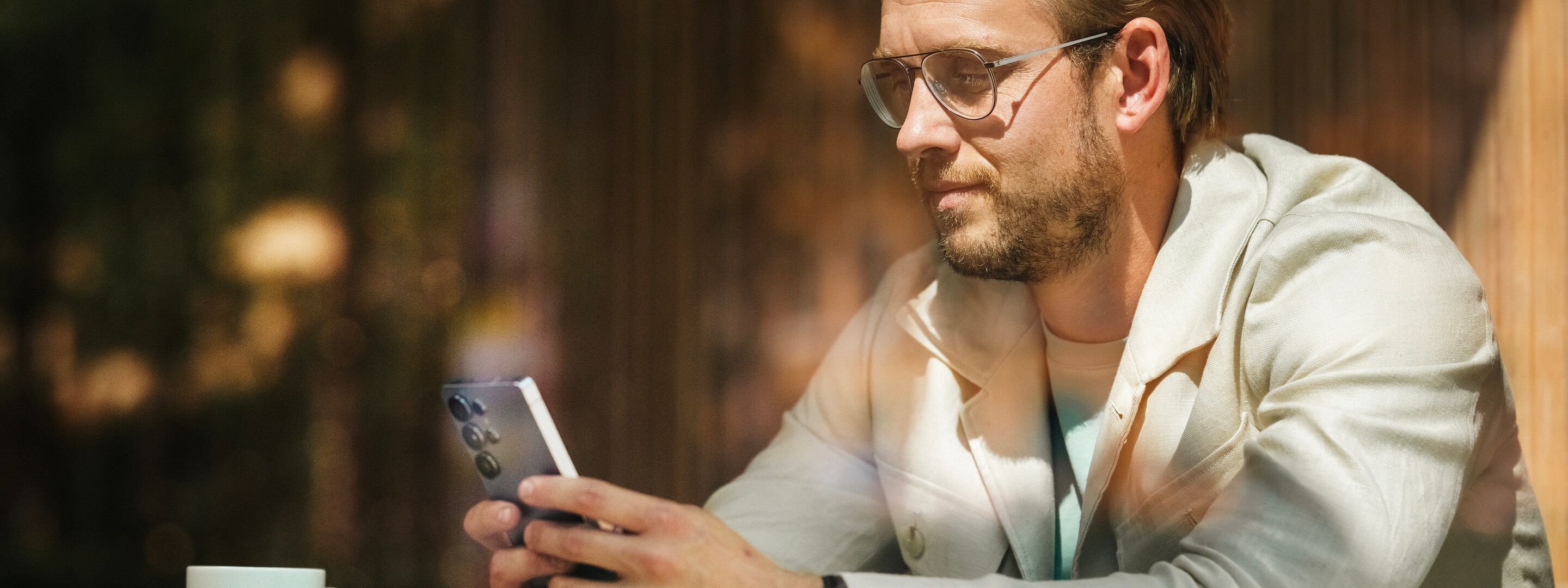 En person holder en mobiltelefon og en kopp står foran