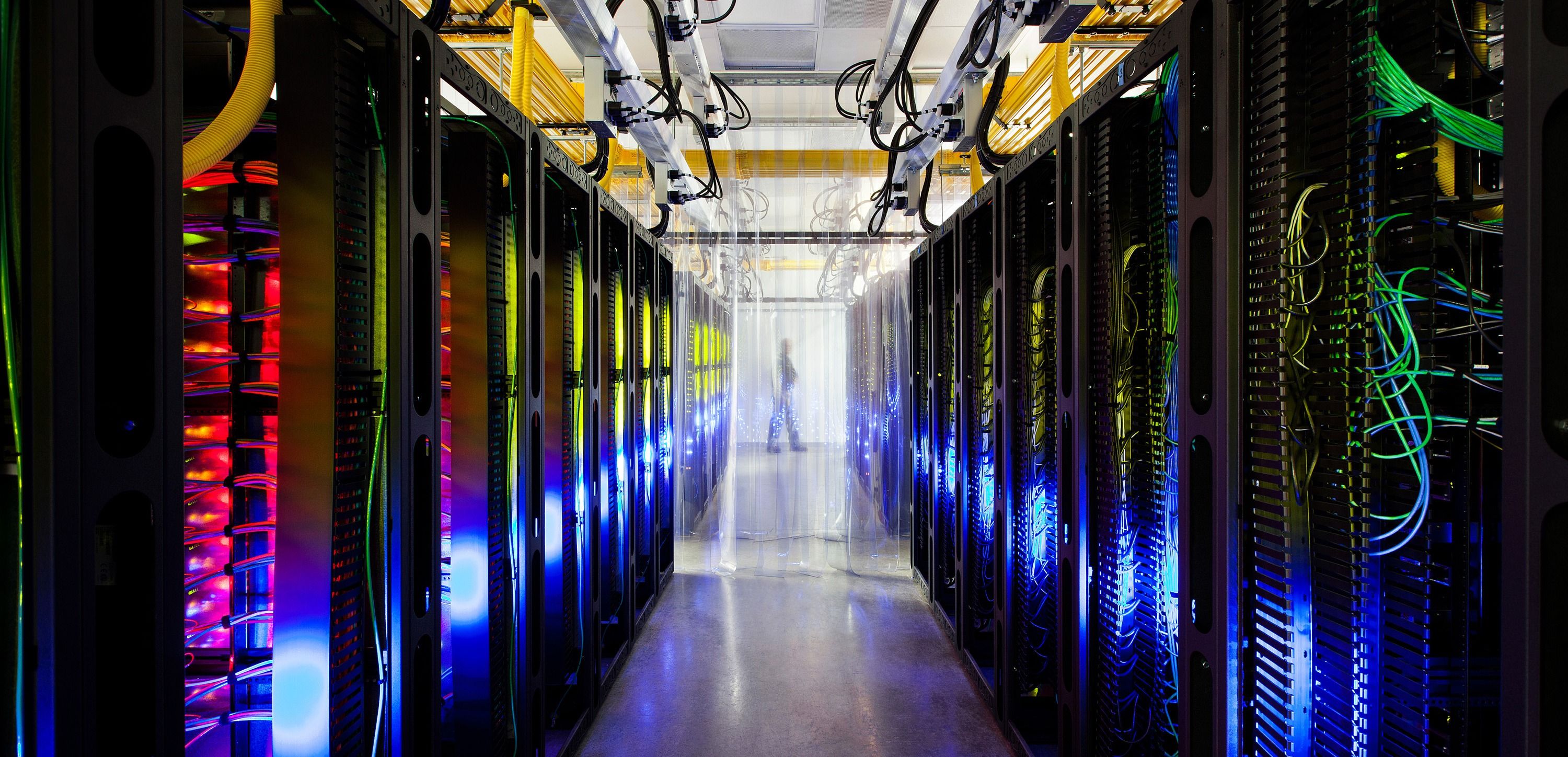 Datasenter med fargerike lys og kabler, person i bakgrunnen