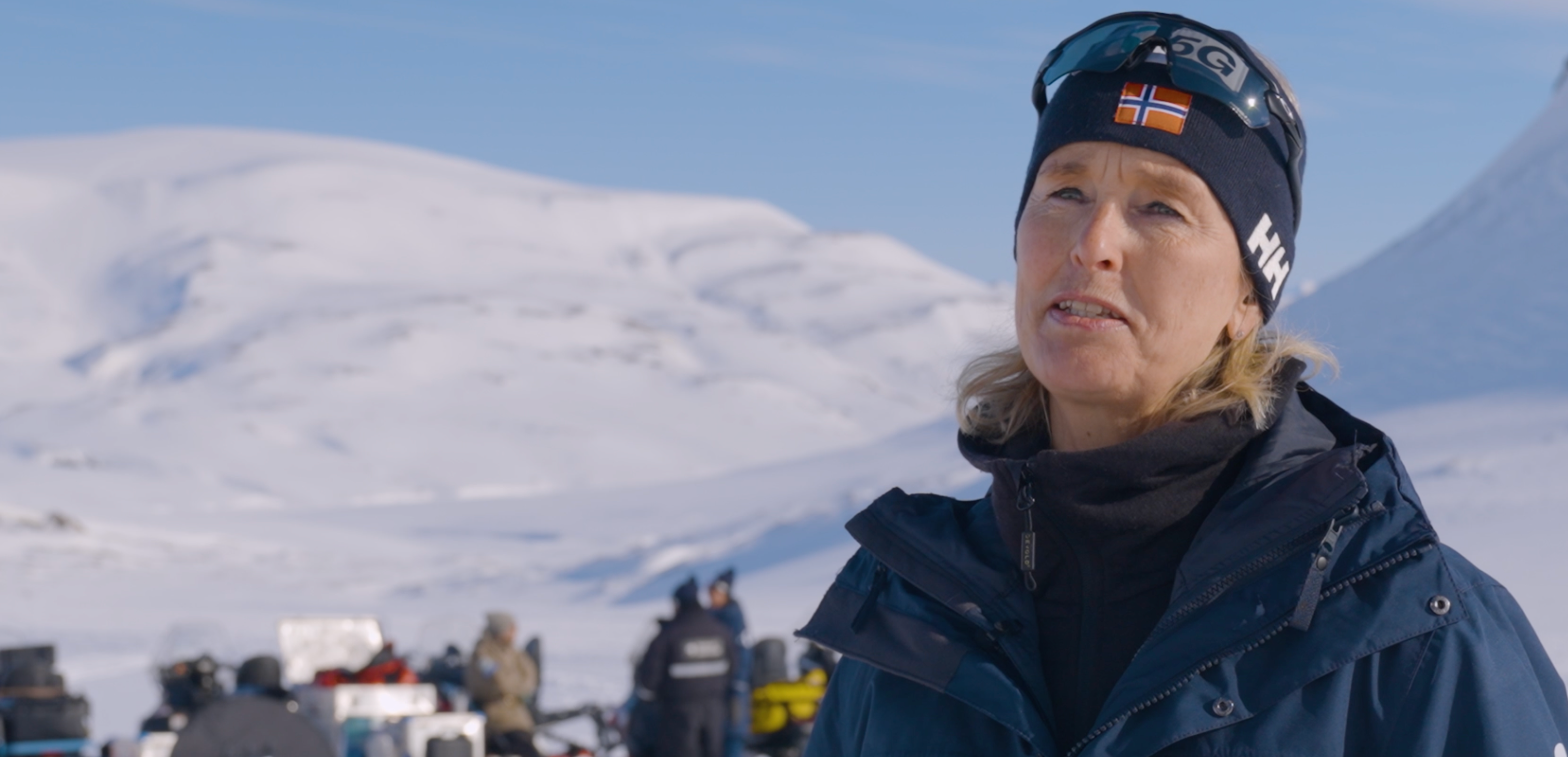 Person med vinterjakke foran snødekt landskap og utstyrsgruppe