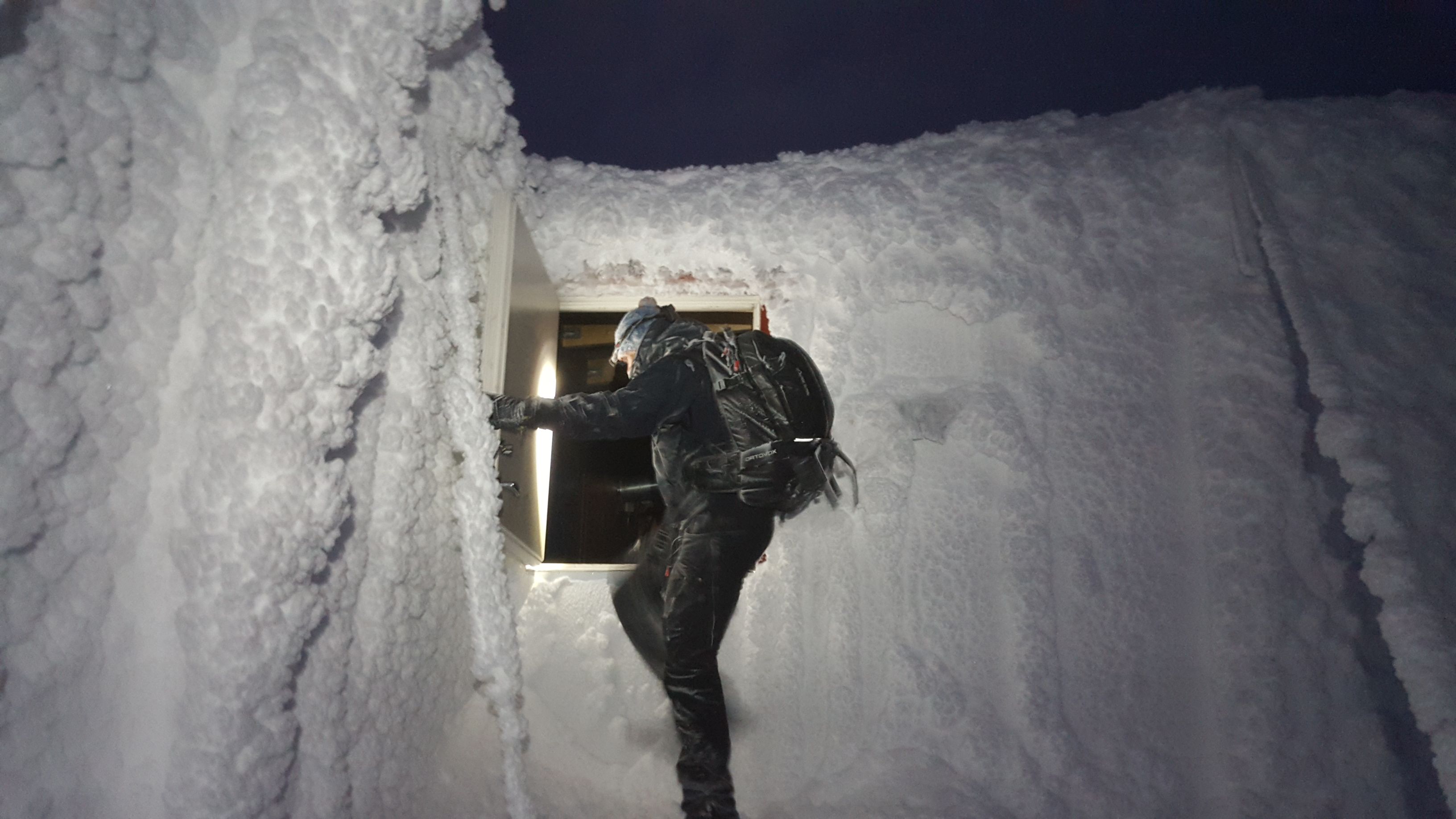 Person klatrer inn i en snødekket bygning gjennom et vindu