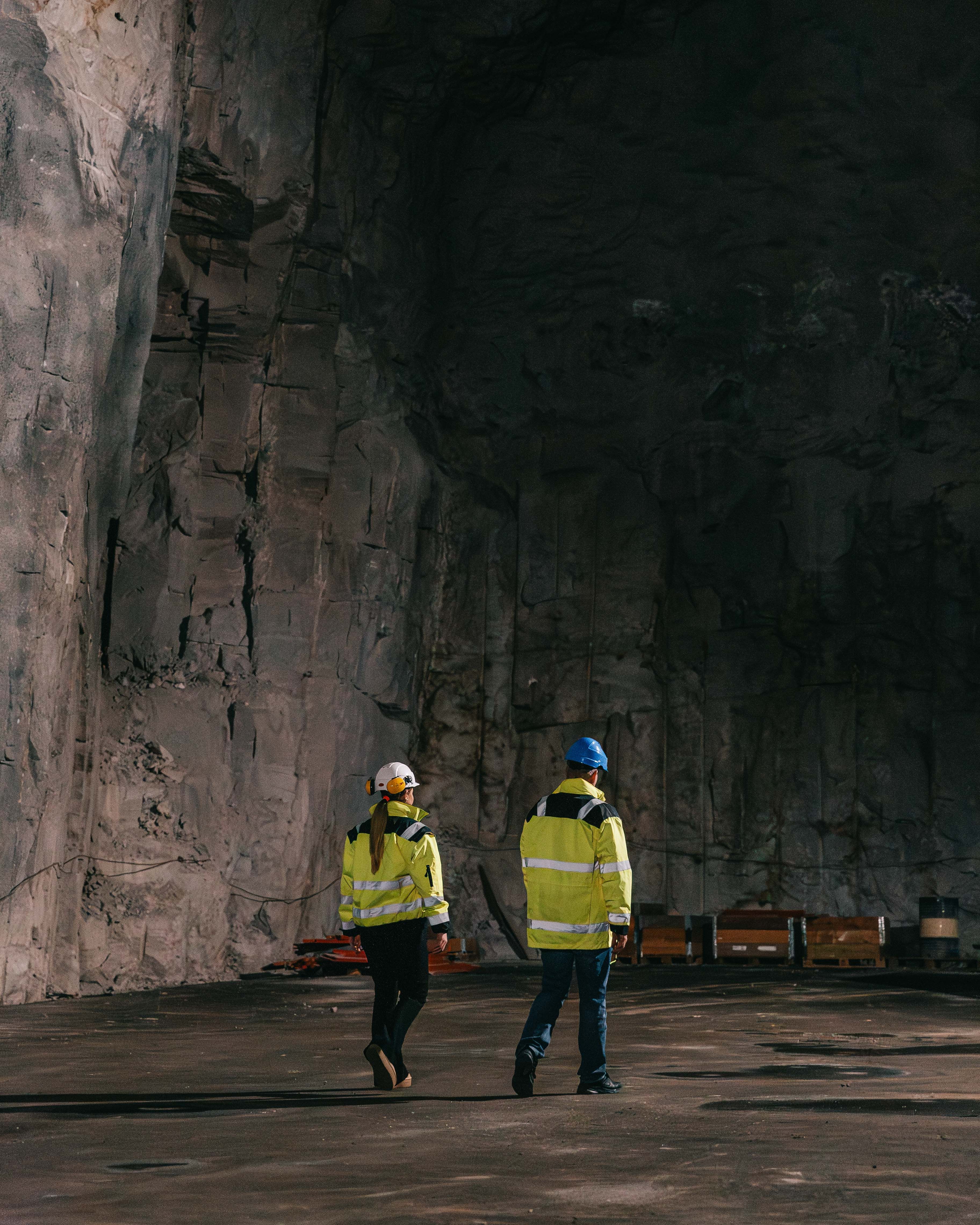 To personer i arbeidsklær og hjelmer i en gruve eller tunnel