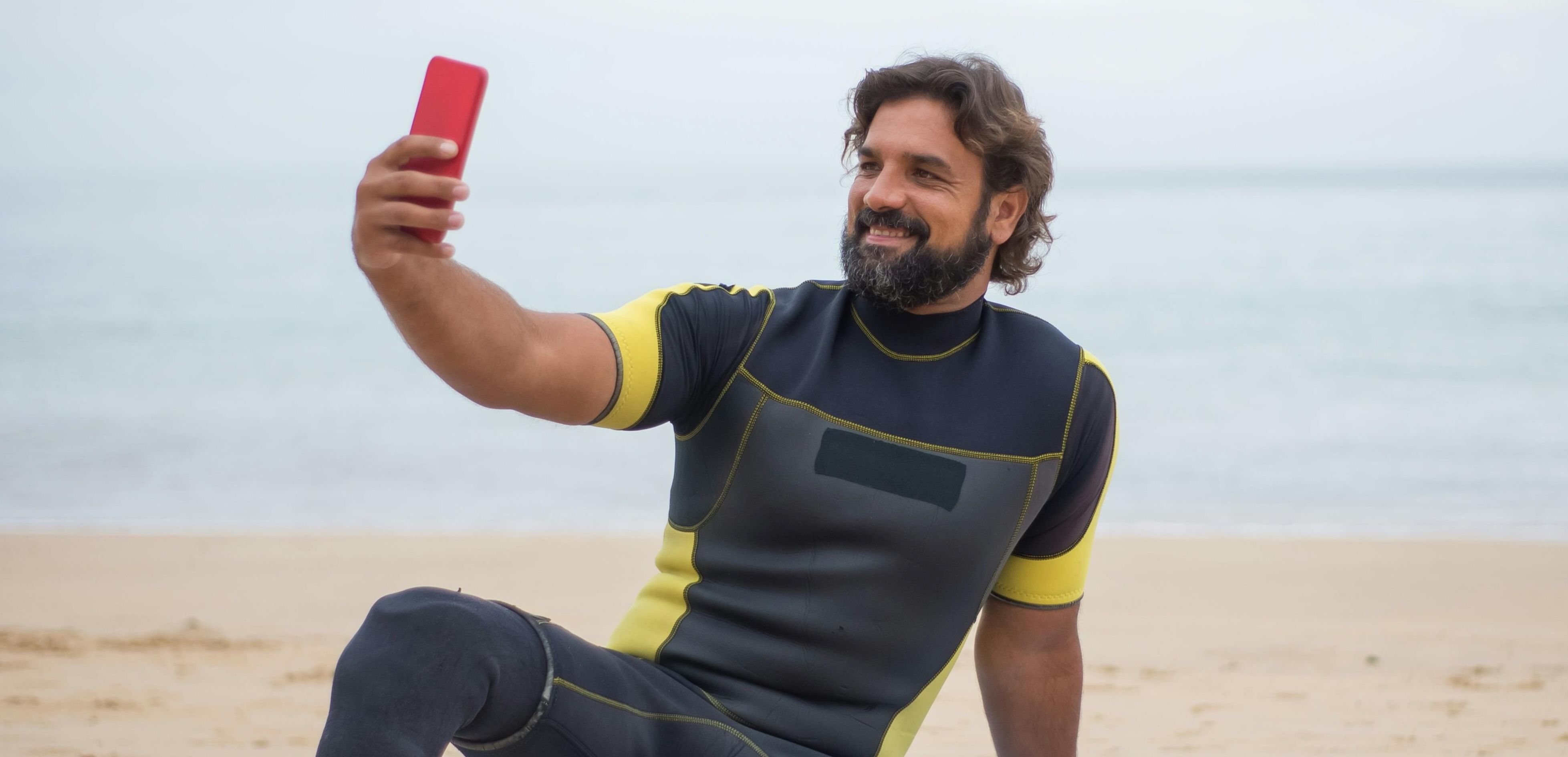 Person i våtdrakt tar en selfie på stranden