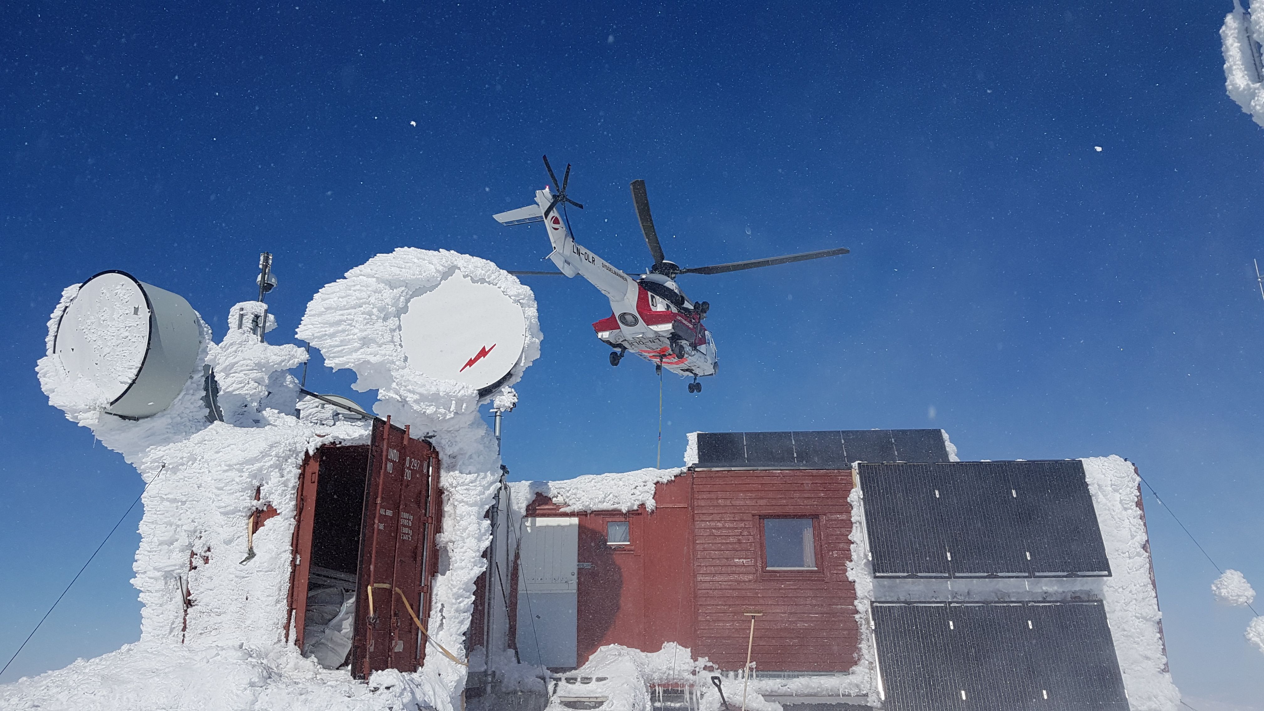 Helikopter svever over snødekt hytte og satellittutstyr