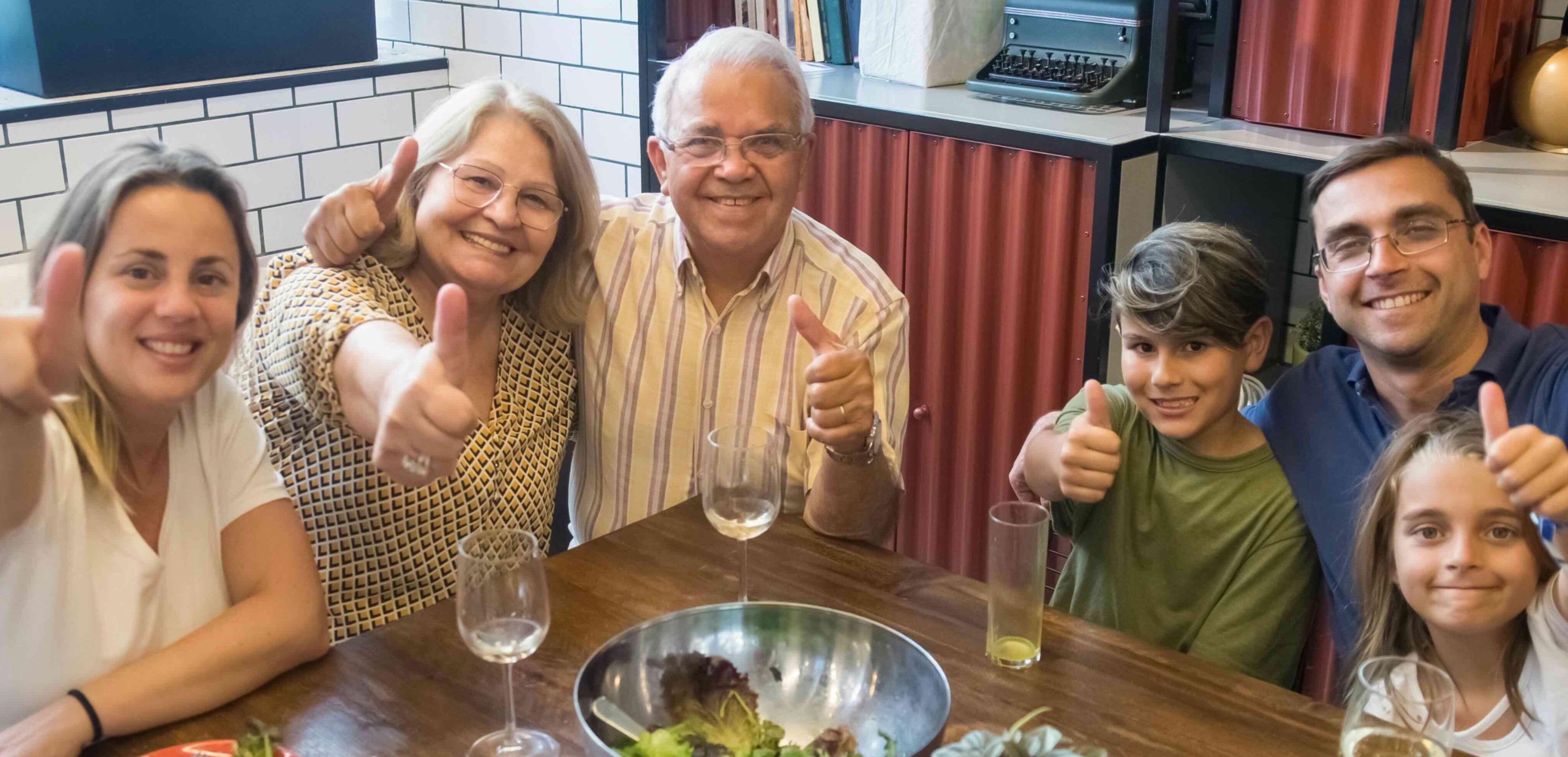 Familie samlet rundt spisebord med tommelen opp