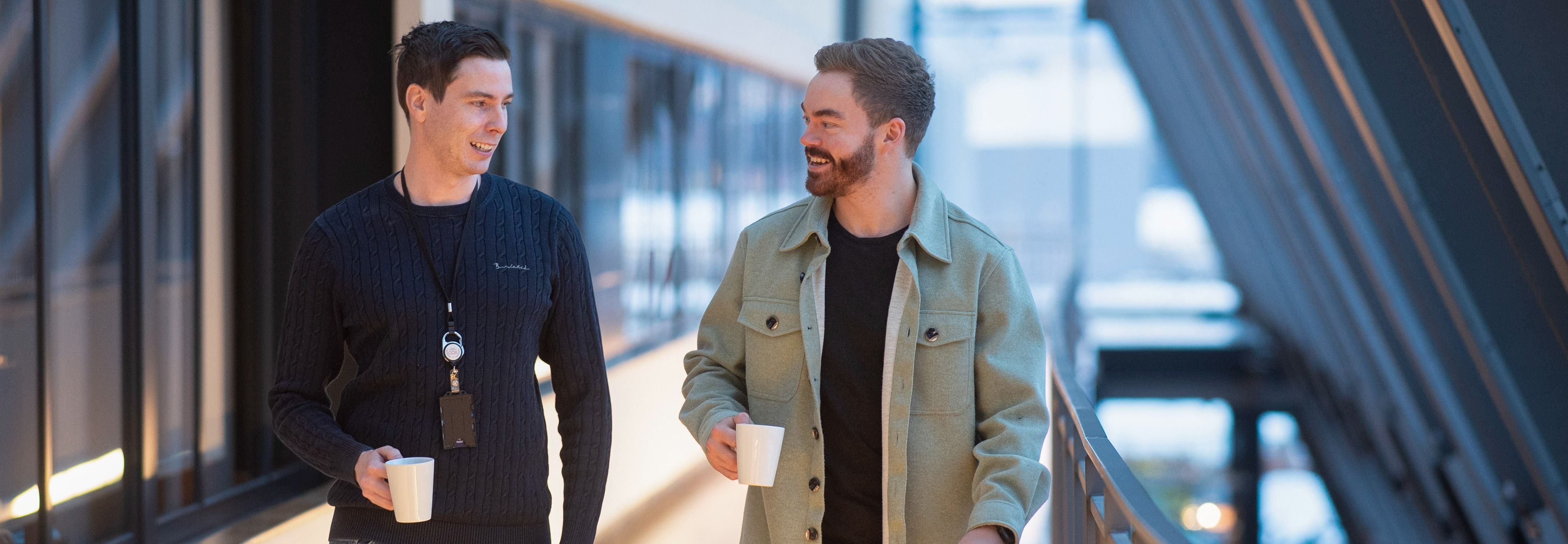 To personer går i gang med kaffekopper i en moderne bygning