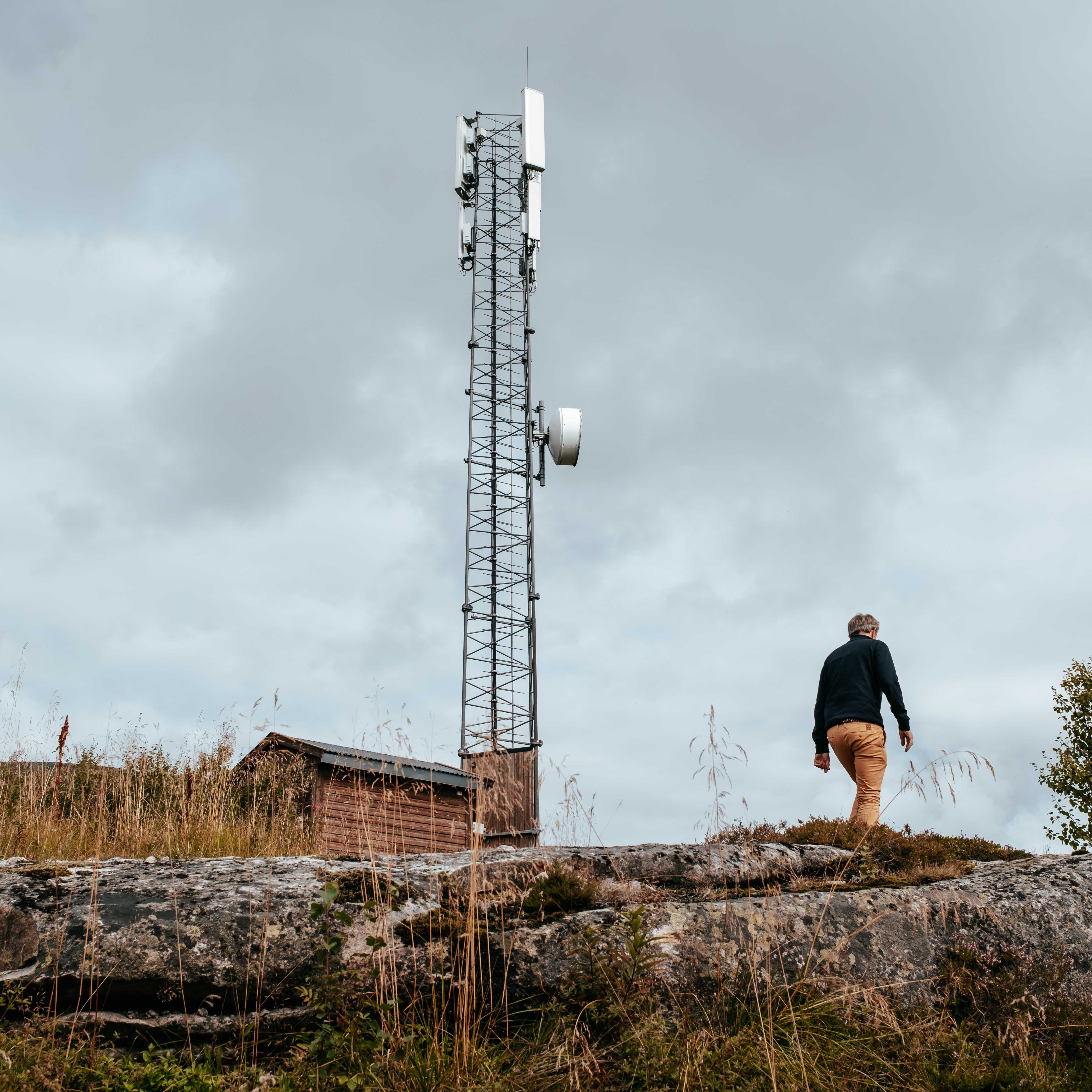 Person går på stein ved siden av en telekommunikasjonsmast