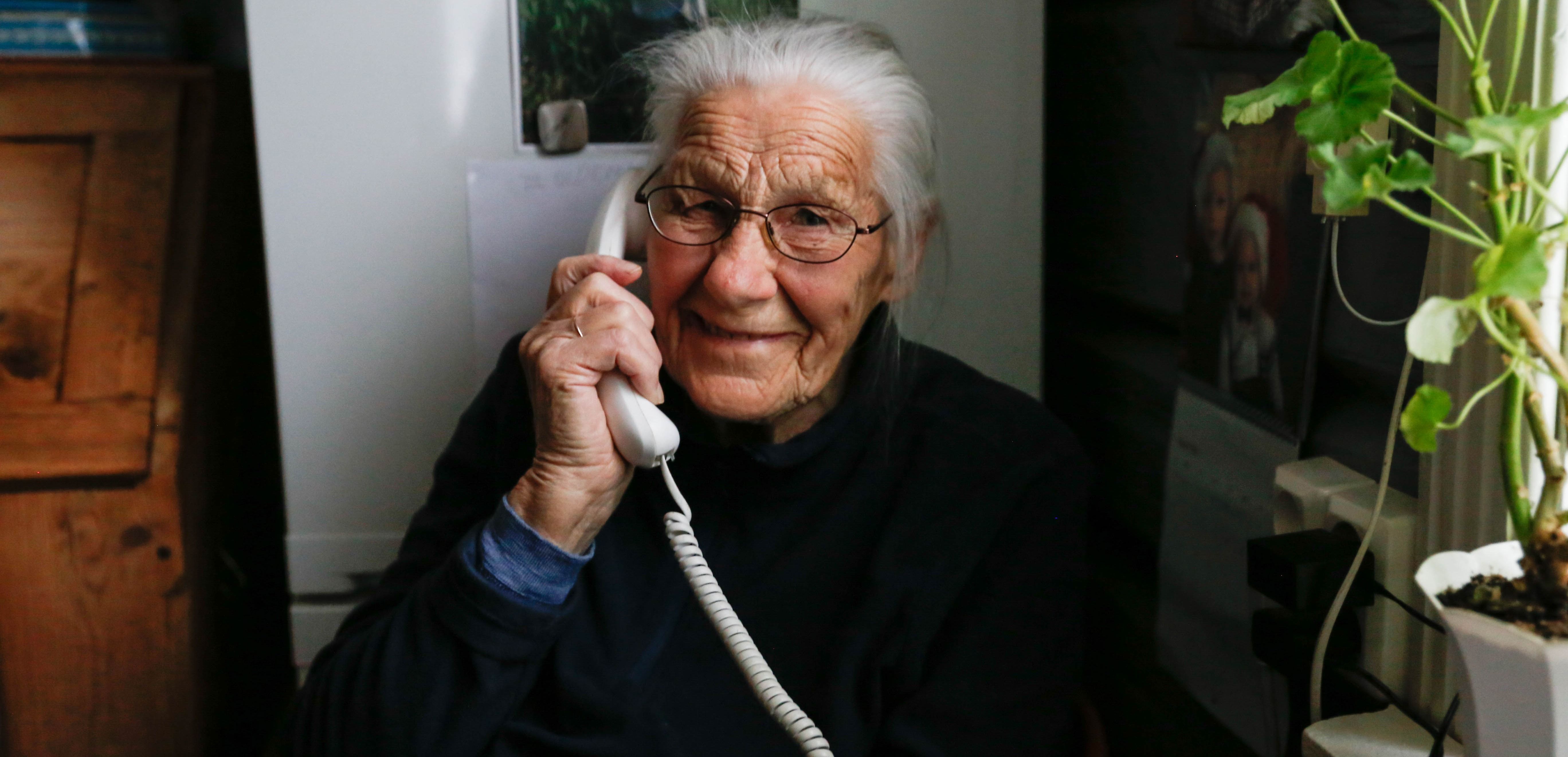 Eldre person holder en telefon ved et bord med planter