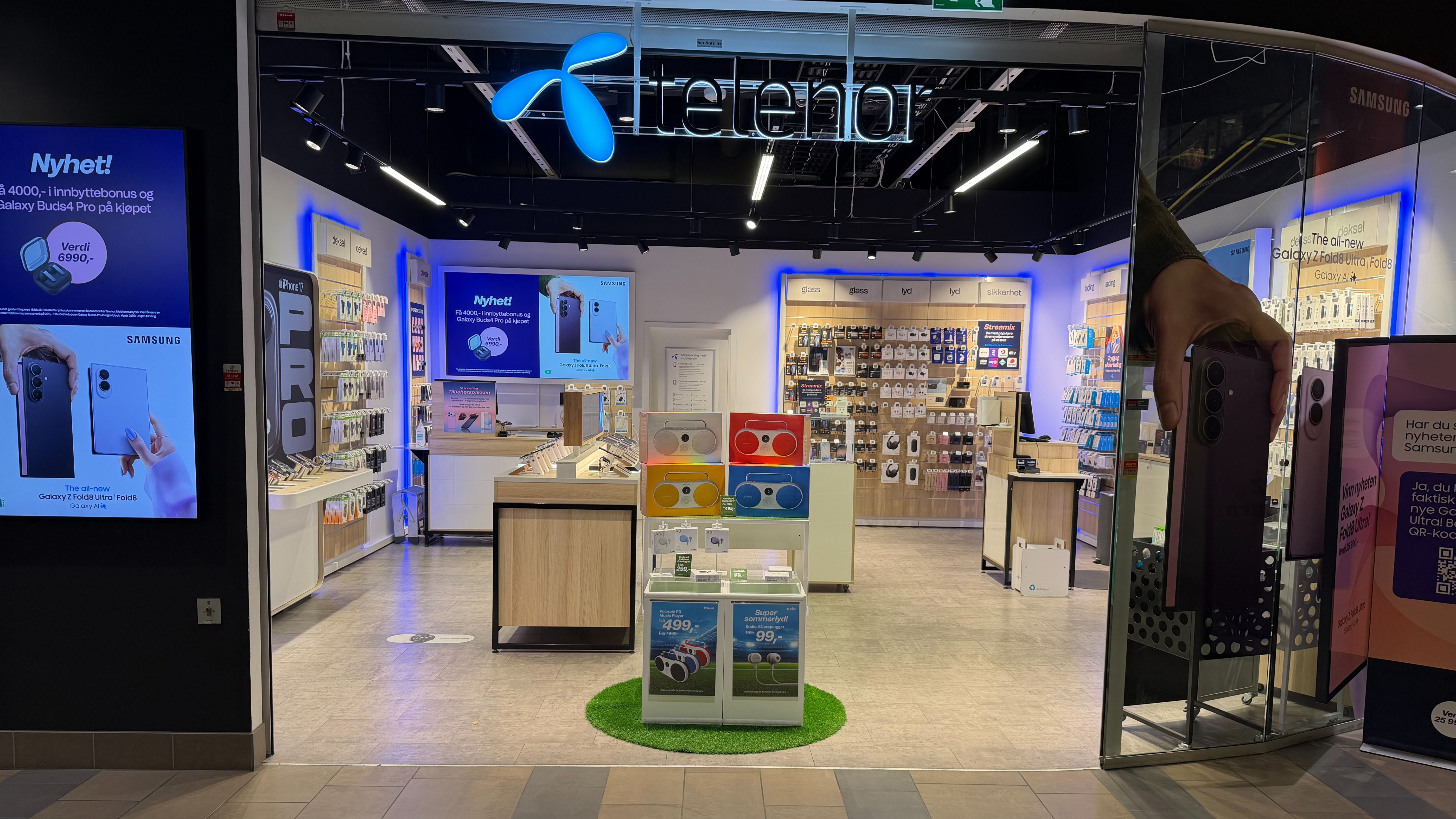 Åpent inngangsparti til en Telenor-butikk med utstilling av mobiler og tilbehør.