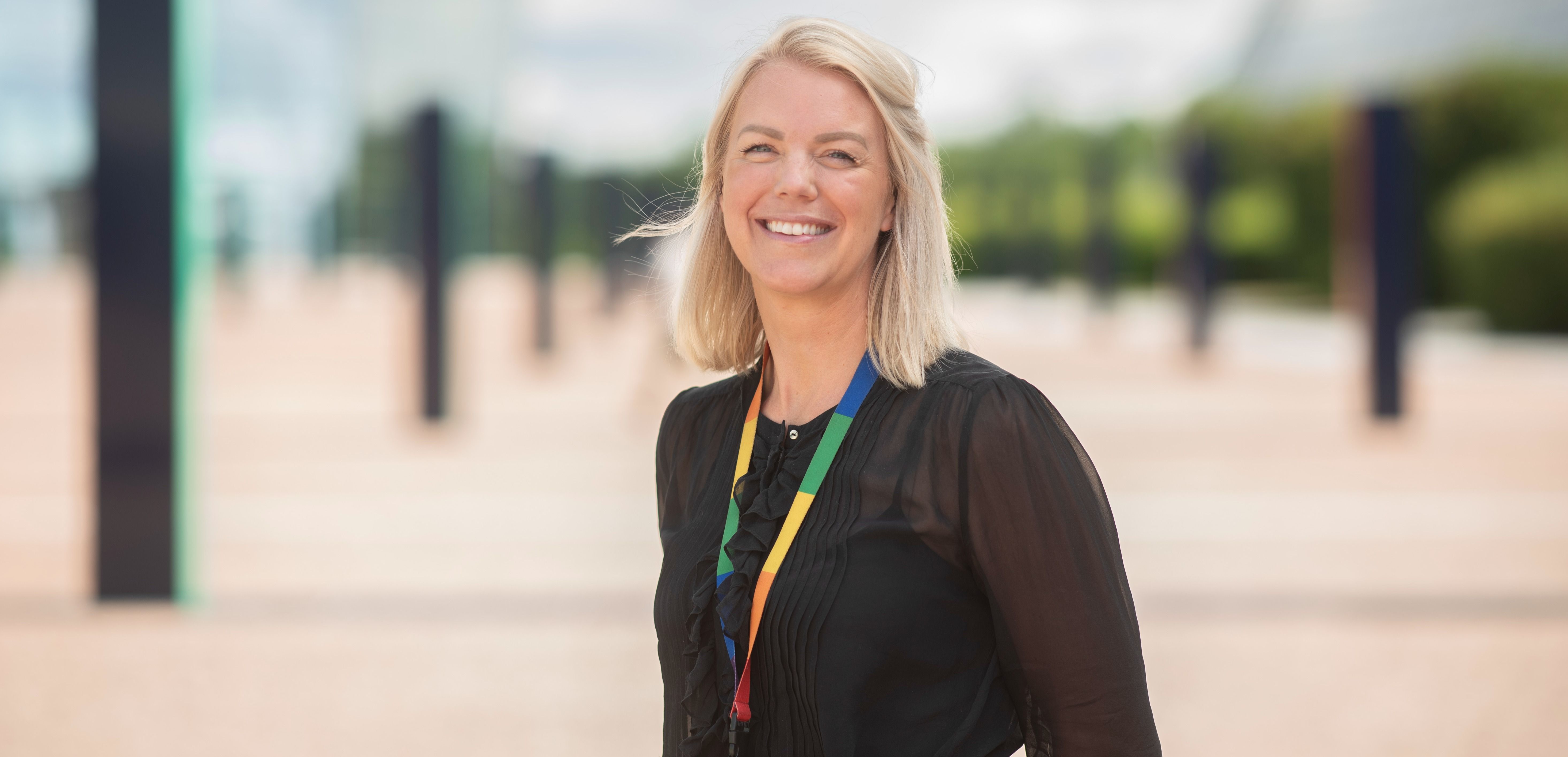 Person med lyst hår iført svart bluse og fargerik snor utendørs