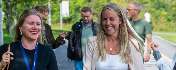 Personer går sammen i et grønt uteområde, noen med arbeidstilbehør