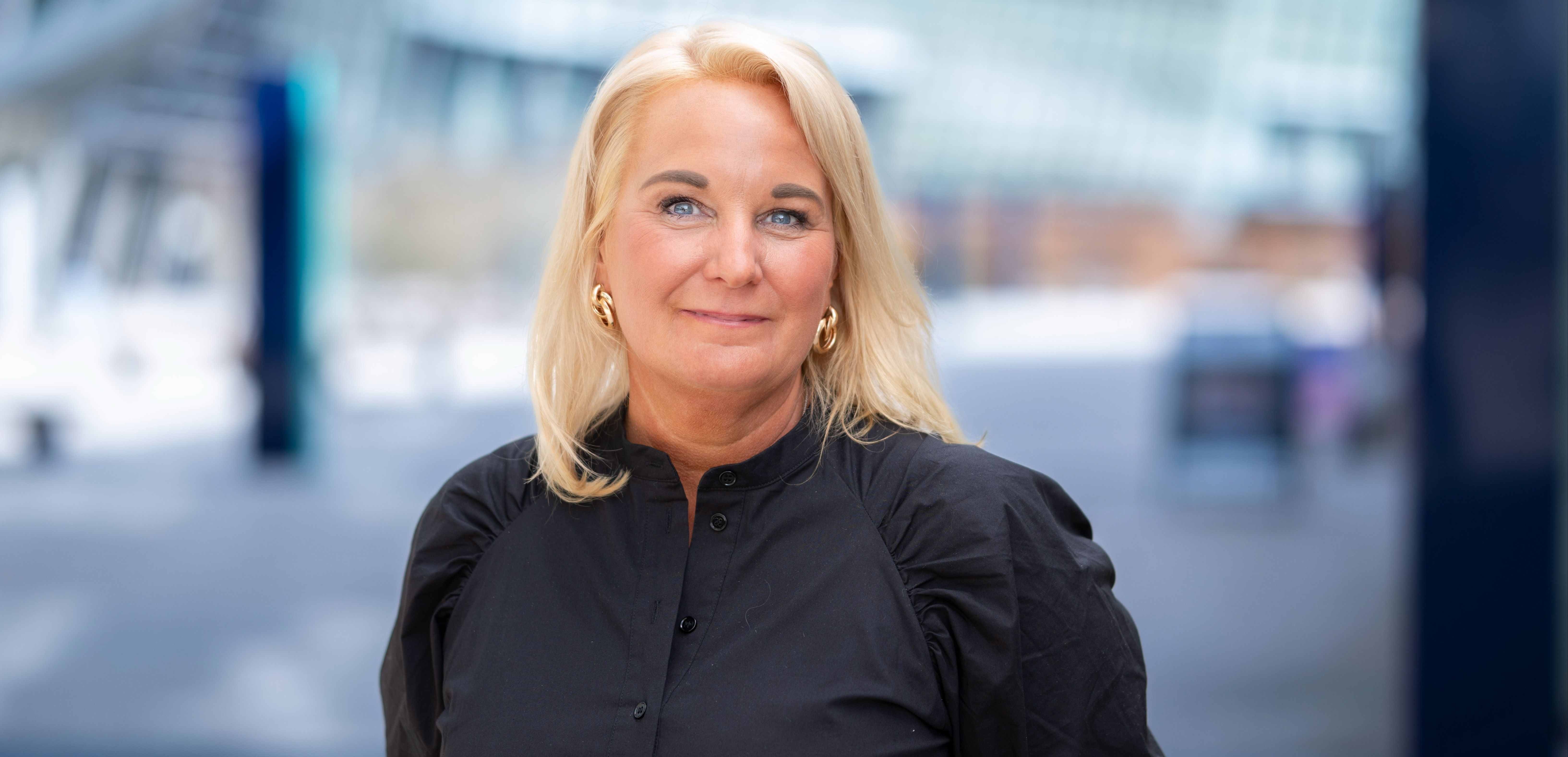 Kvinne i beige bluse foran grønne planter