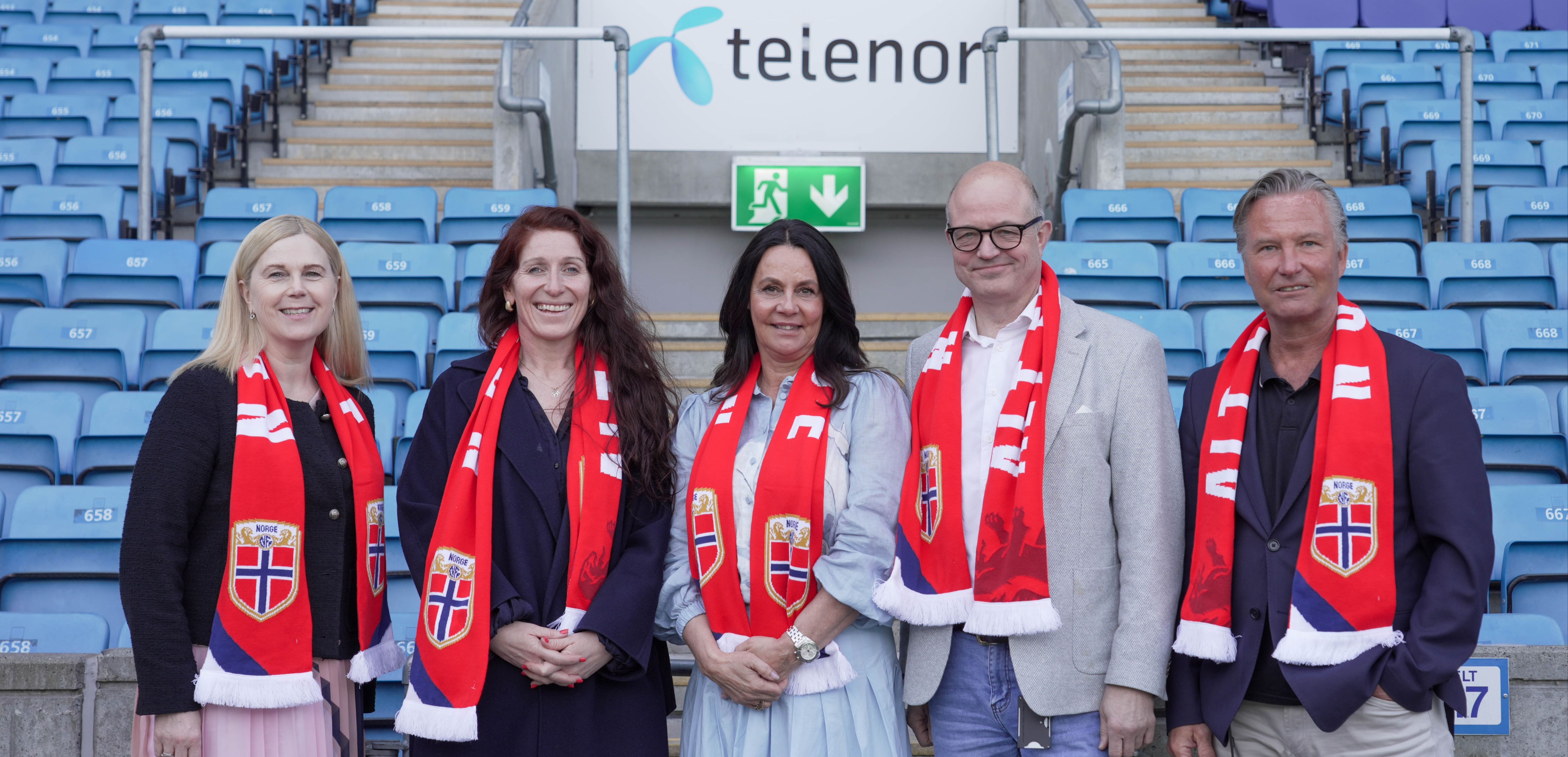 Fem personer med røde skjerf foran blå stadionseter
