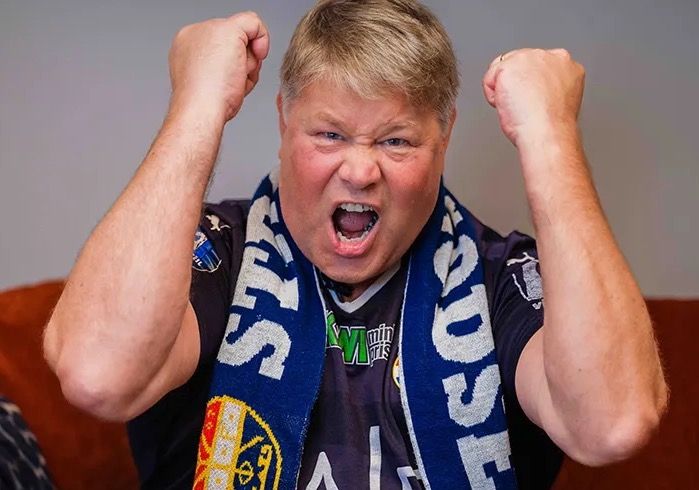 Mann med Strømsgodset-skjerf jubler i sofaen fordi ha in ikke har dårlig wifi