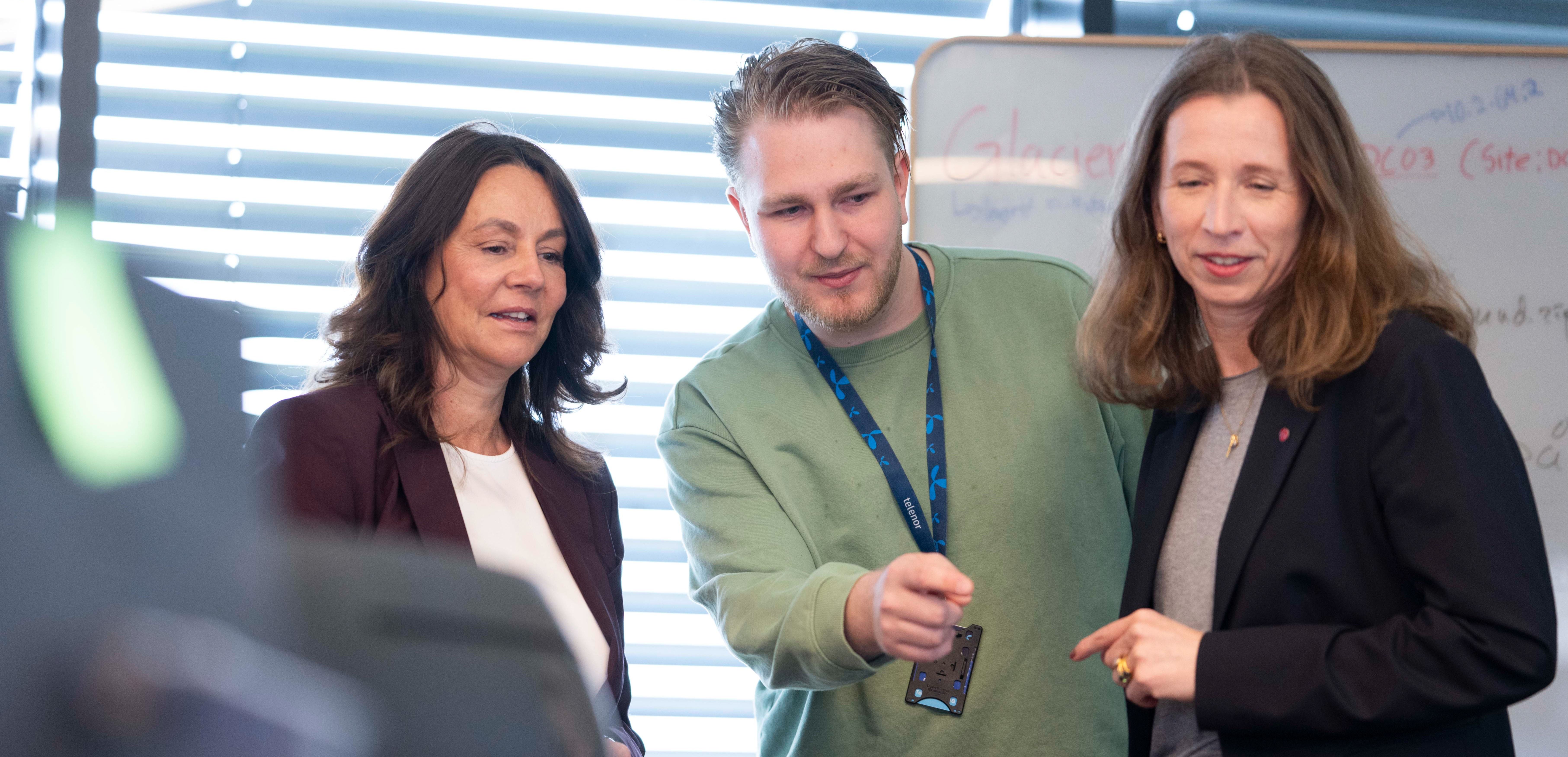 Tre personer diskuterer foran en tavle med notater