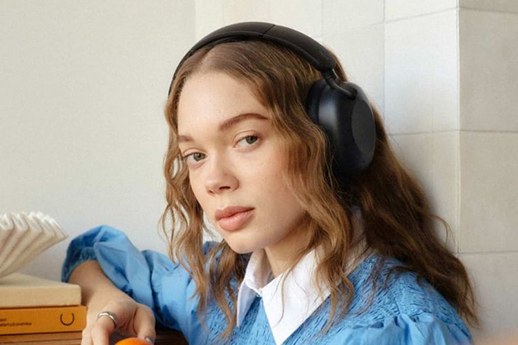 jente med sudio k2 hodetelefoner, blå genser og bøker i bakgrunnen