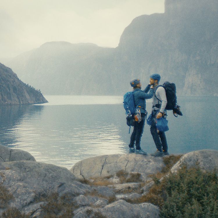 To personer med klatreutstyr ved en fjord og fjell i bakgrunnen