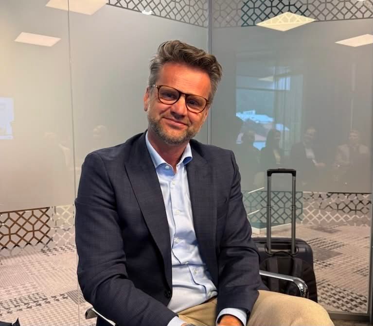 Mann i dress på kontor med koffert i bakgrunnen