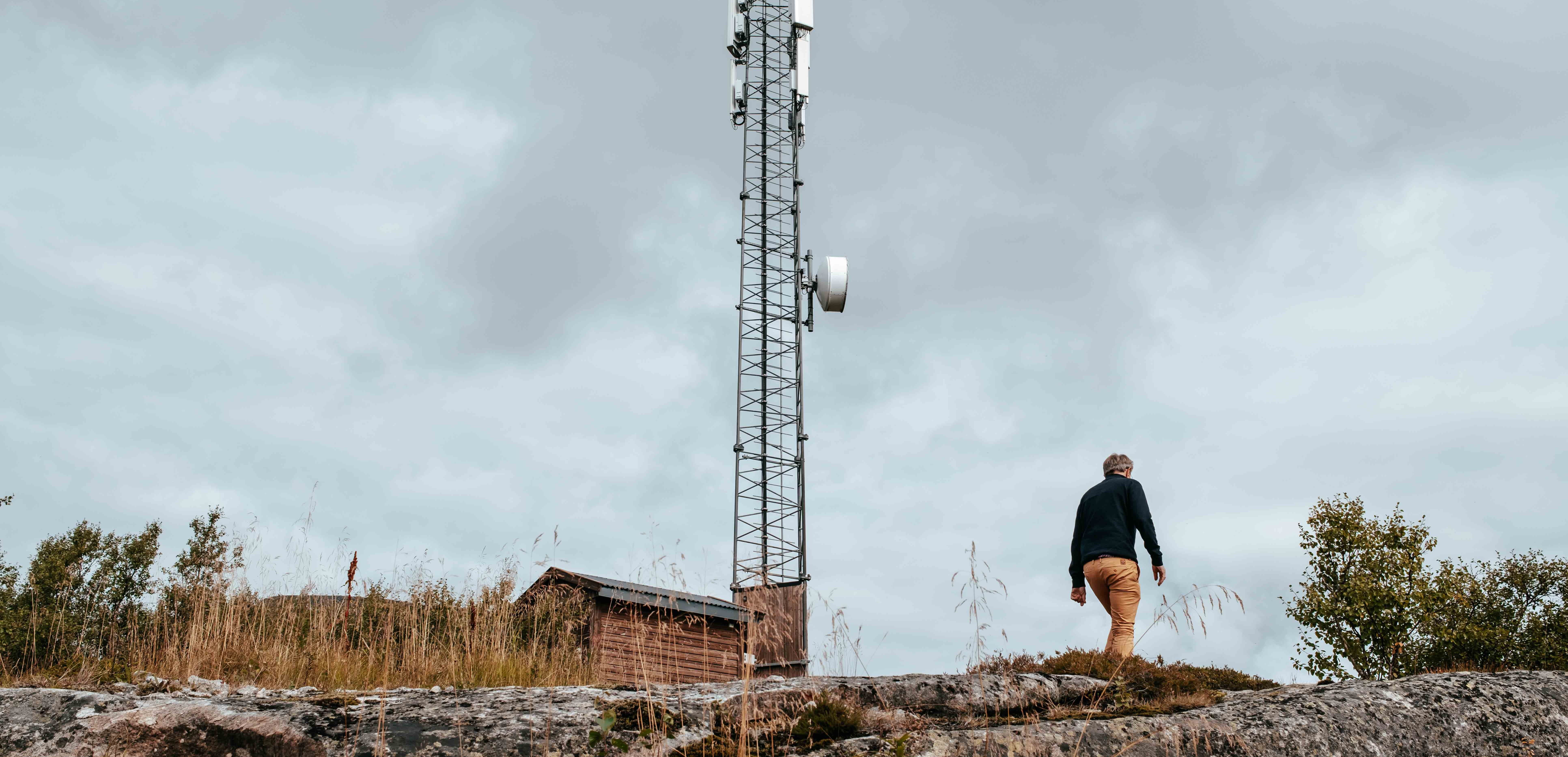 Person går på steinete bakke ved siden av en telekommunikasjonstower