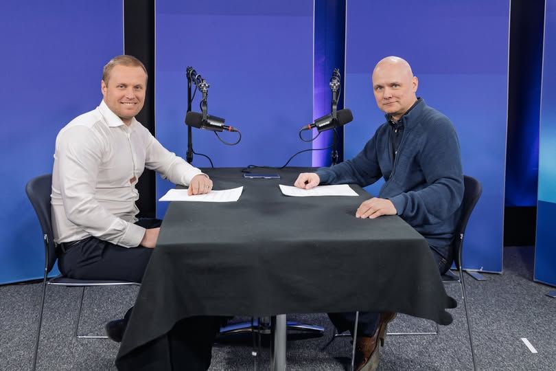 To personer sitter ved et bord med mikrofoner, klar for podkastinnspilling