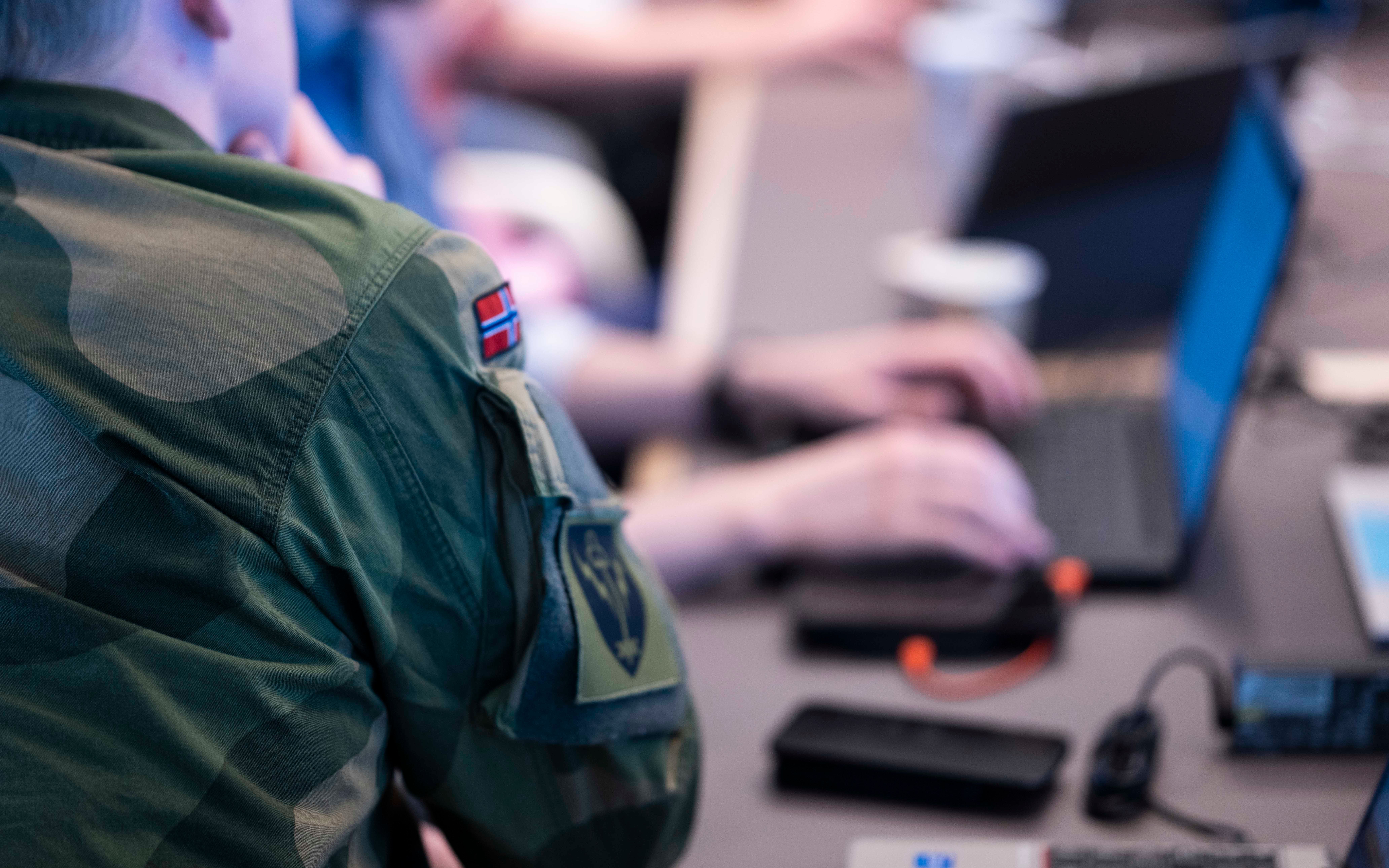 Soldat i norsk uniform ved skrivebord med laptop og utstyr