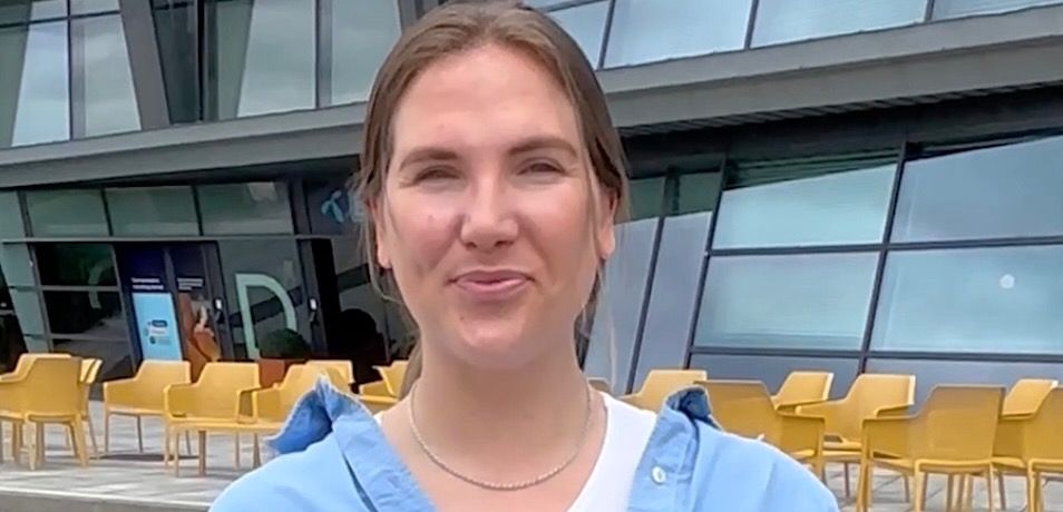 Person foran moderne bygning med gule stoler og grønne busker