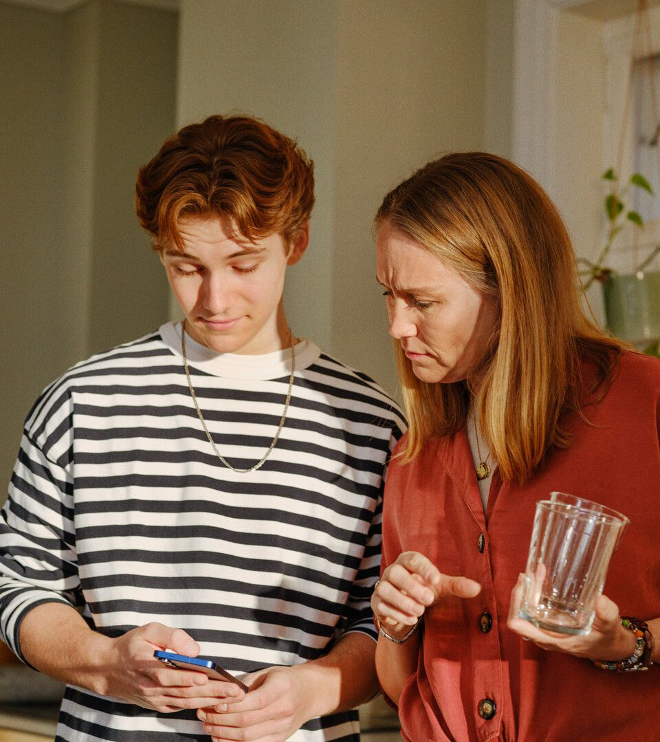 To personer i et lyst rom, holder mobil og glass