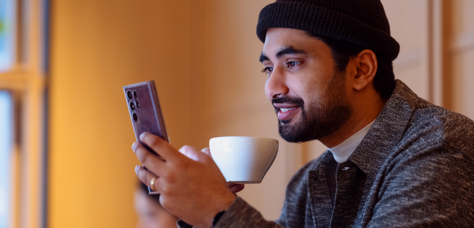 Person sitter med mobil og kaffekopp i en avslappet kafésetting