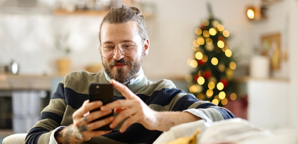 Mann i stua med juletre ser på mobilen sin