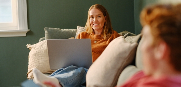 Person sitter på sofa med laptop foran seg, hyggelig innemiljø