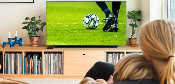 Mor og barn ser på fotballkamp på TV hjemme, og de kan gjøre opptak av fotball-VM.