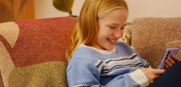 Jente med mobil sitter i en sofa
