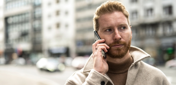 En alvorlig mann med skjegg snakker i mobiltelefonen på en gate i byen.